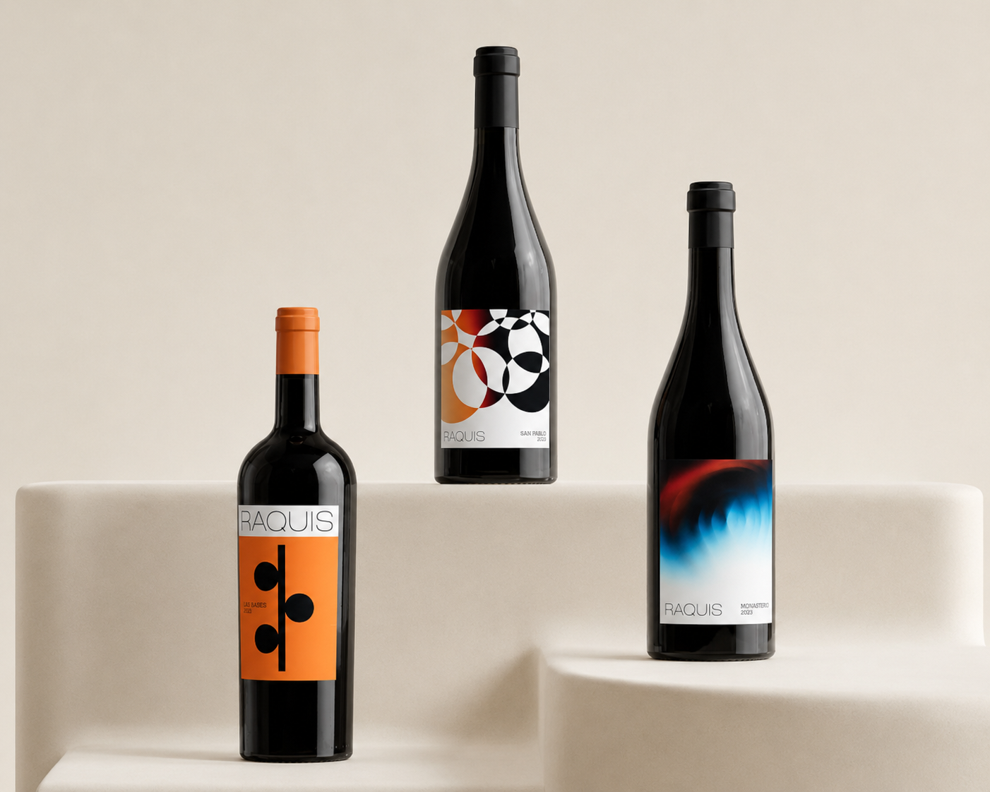 Three Raquis bottles — Las Bases, San Pablo and Monasterio — on a warm studio ground